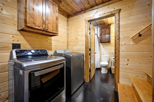 clothes washing area with wood walls, washing machine and clothes dryer, wooden ceiling, and cabinet space