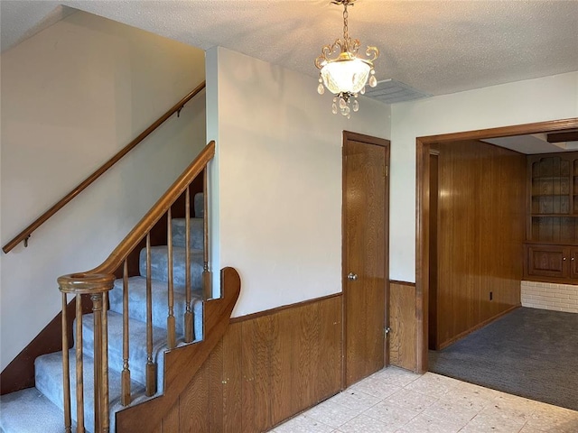 10900 Willow Grove Rd, Oklahoma City, OK 73120 - staircase featuring wood walls, tile patterned floors, a wainscoted wall, a chandelier, and a textured ceiling