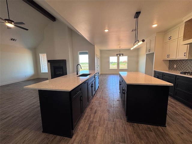 kitchen featuring visible vents, a sink, dark cabinetry, and a center island with sink