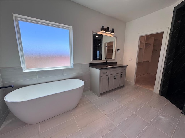 bathroom featuring a walk in closet, tile walls, vanity, tile patterned floors, and a soaking tub