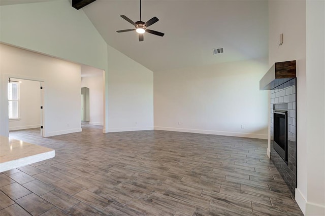 9321 NW 147th Ter, Yukon, OK 73099 - unfurnished living room with high vaulted ceiling, a tile fireplace, ceiling fan, wood finished floors, and beamed ceiling