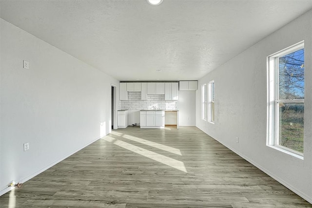 unfurnished living room featuring light wood-type flooring, baseboards, and a textured ceiling