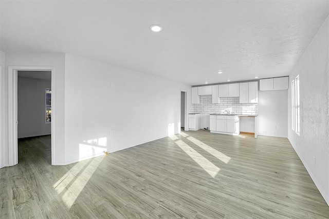 unfurnished living room featuring baseboards, light wood-style floors, and a sink