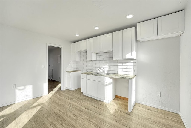 kitchen featuring baseboards, light wood-type flooring, a sink, white cabinetry, and tasteful backsplash