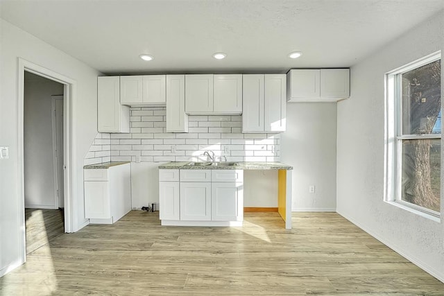 kitchen with backsplash, light wood-style flooring, white cabinetry, and baseboards