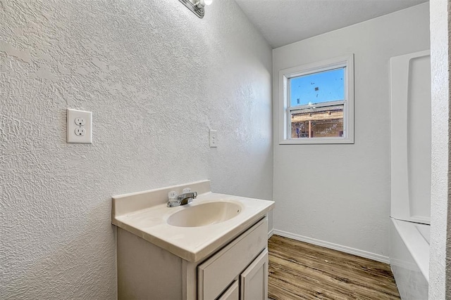 bathroom featuring baseboards, vanity, a textured wall, wood finished floors, and a textured ceiling