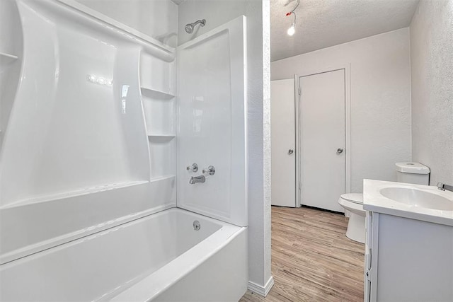 full bath with toilet, a textured ceiling, wood finished floors,  shower combination, and a textured wall