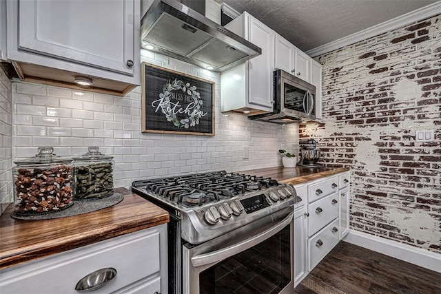 kitchen featuring butcher block countertops, backsplash, appliances with stainless steel finishes, and wall chimney exhaust hood