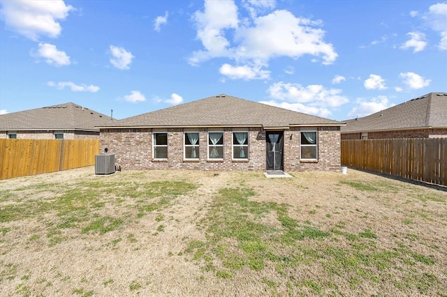 rear view of house with cooling unit, a fenced backyard, brick siding, and a shingled roof