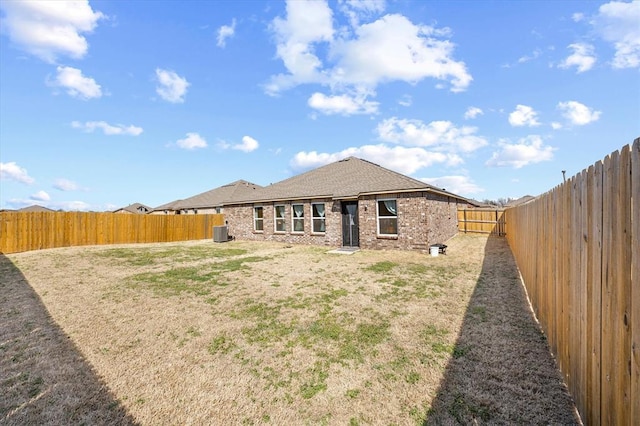 back of house with brick siding, a shingled roof, central air condition unit, a lawn, and a fenced backyard