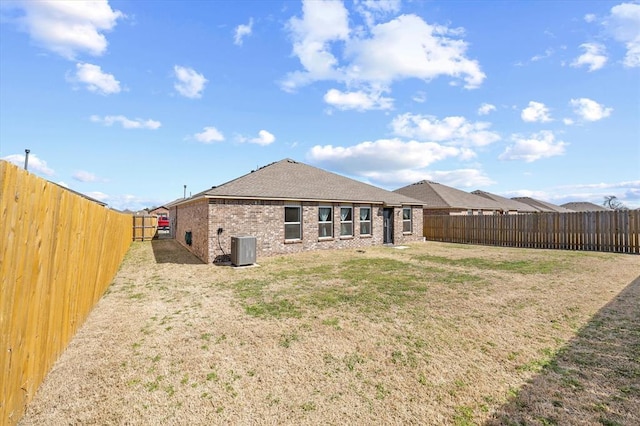 back of property with a lawn, a fenced backyard, and central AC