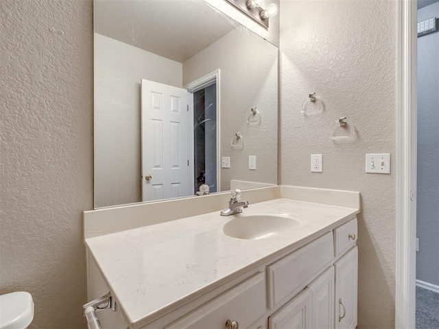 bathroom featuring toilet, vanity, and a textured wall