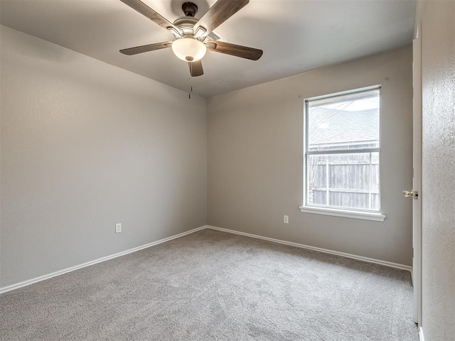 carpeted spare room featuring baseboards and a ceiling fan