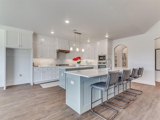 kitchen featuring stainless steel appliances, white cabinets, arched walkways, a large island with sink, and light countertops