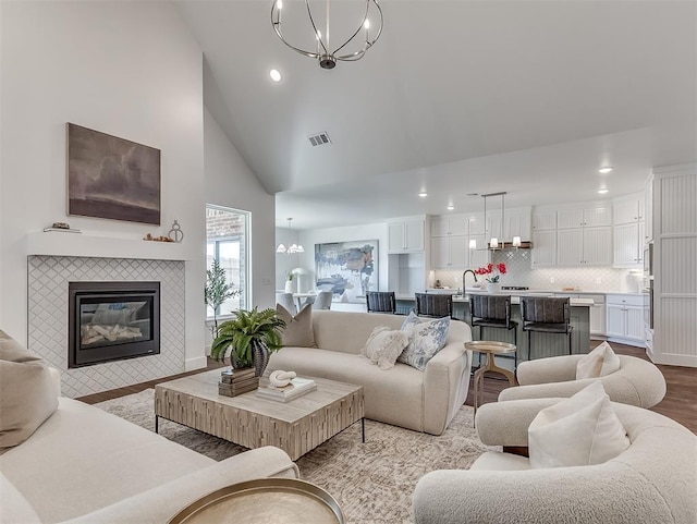 living area with a chandelier, recessed lighting, light wood-style floors, high vaulted ceiling, and a tiled fireplace