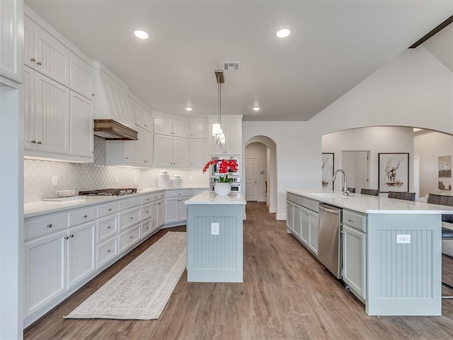 kitchen featuring a center island with sink, appliances with stainless steel finishes, arched walkways, light countertops, and vaulted ceiling