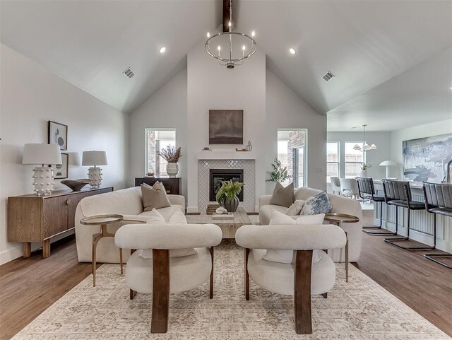 living room with a chandelier, high vaulted ceiling, wood finished floors, a tile fireplace, and recessed lighting