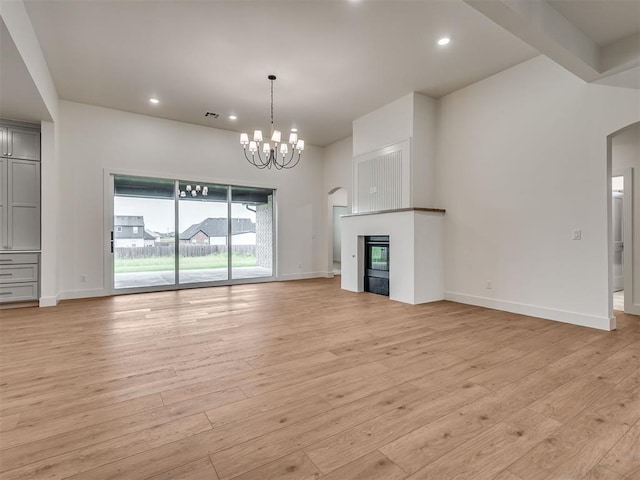 77 Orchid Ct, Piedmont, OK 73078 - unfurnished living room with a chandelier, light wood-type flooring, a glass covered fireplace, recessed lighting, and arched walkways