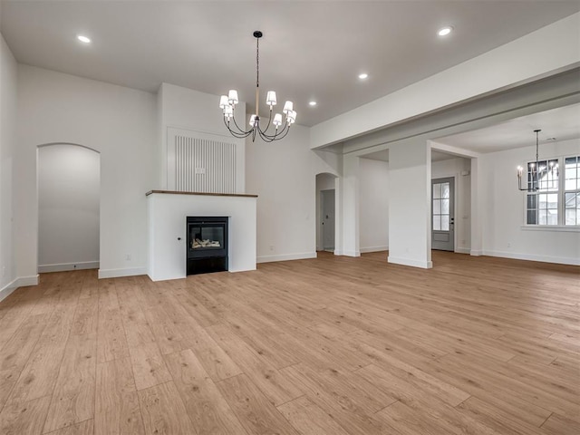77 Orchid Ct, Piedmont, OK 73078 - unfurnished living room featuring a chandelier, arched walkways, light wood-type flooring, a glass covered fireplace, and recessed lighting