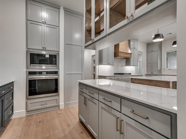 77 Orchid Ct, Piedmont, OK 73078 - kitchen featuring appliances with stainless steel finishes, gray cabinets, premium range hood, light wood finished floors, and light stone countertops