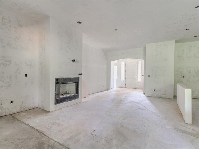 9070 Oak Tree Cir, Edmond, OK 73025 - unfurnished living room featuring arched walkways, a fireplace, and unfinished concrete floors