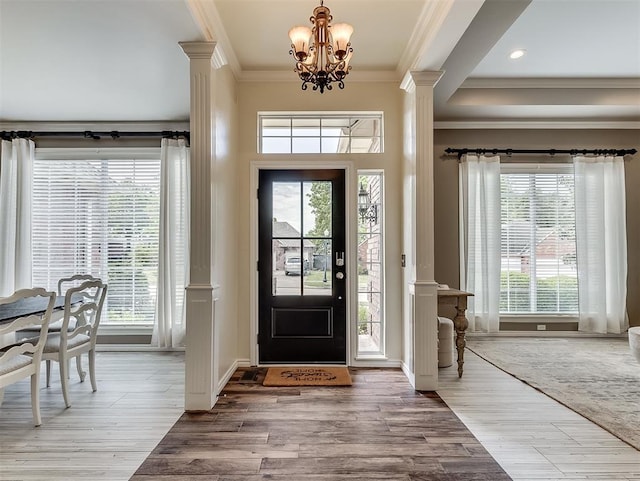 entrance foyer featuring crown molding, wood finished floors, decorative columns, and a chandelier