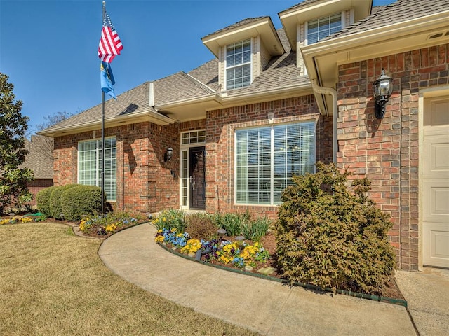 property entrance featuring roof with shingles, a yard, and brick siding