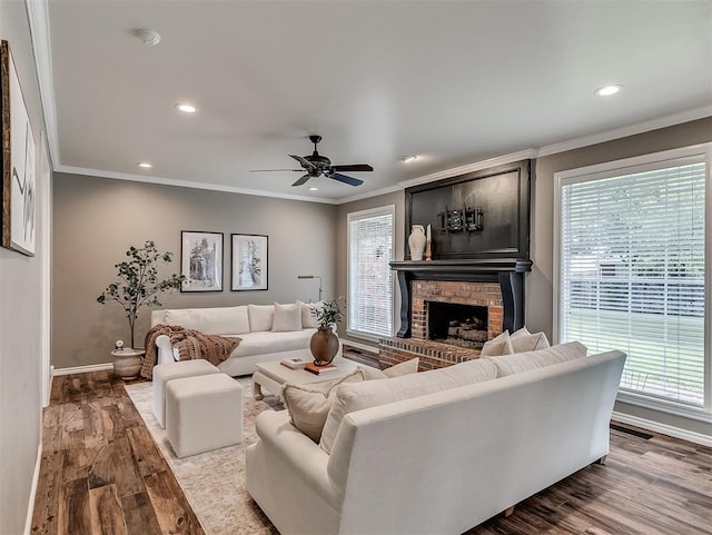living area featuring wood finished floors, recessed lighting, ornamental molding, and a brick fireplace