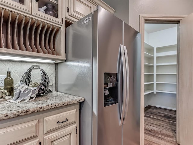 kitchen with decorative backsplash, glass insert cabinets, stainless steel fridge, light stone counters, and wood finished floors