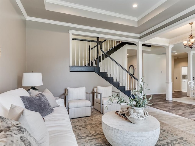 living area featuring wood finished floors, stairs, ornamental molding, a notable chandelier, and a tray ceiling