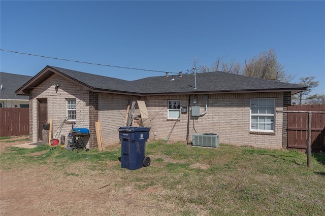 rear view of house featuring brick siding, central AC unit, fence, and a lawn