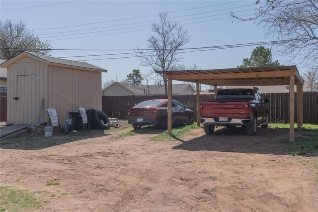 view of yard featuring an outdoor structure, a shed, fence, dirt driveway, and a carport