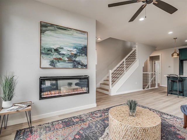 living area with light wood-type flooring, stairway, and ceiling fan