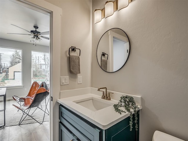 bathroom featuring toilet, vanity, wood finished floors, ceiling fan, and a textured wall