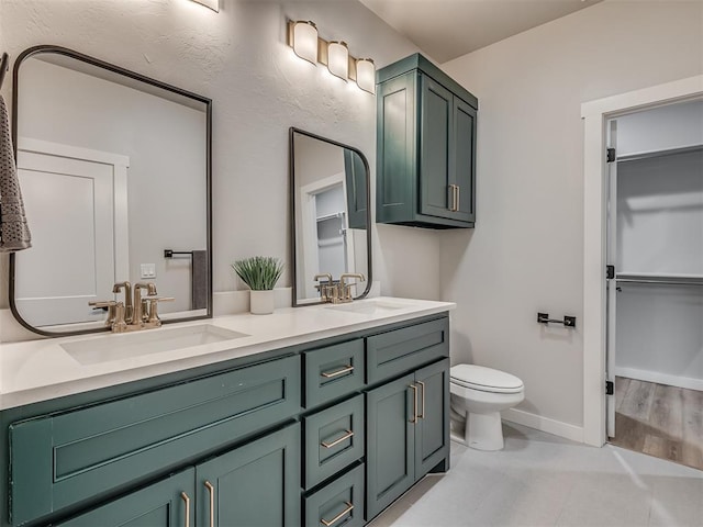 full bathroom with toilet, double vanity, a sink, and baseboards