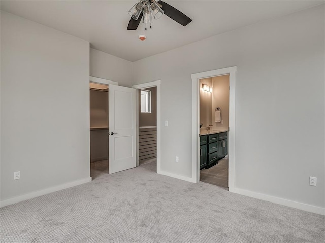 unfurnished bedroom featuring connected bathroom, a closet, light carpet, a spacious closet, and baseboards
