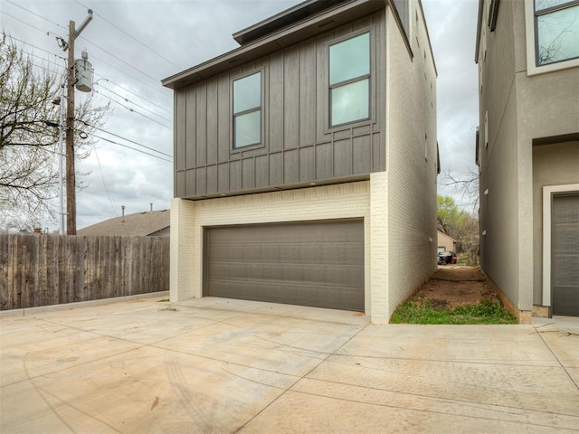 view of front facade featuring fence, an attached garage, board and batten siding, driveway, and brick siding