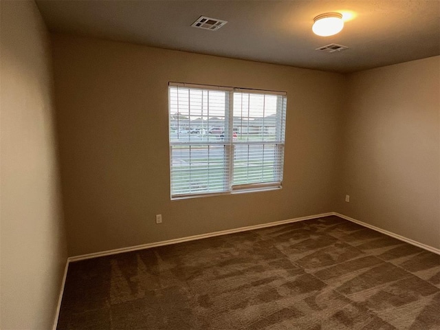 spare room featuring visible vents, baseboards, and dark colored carpet