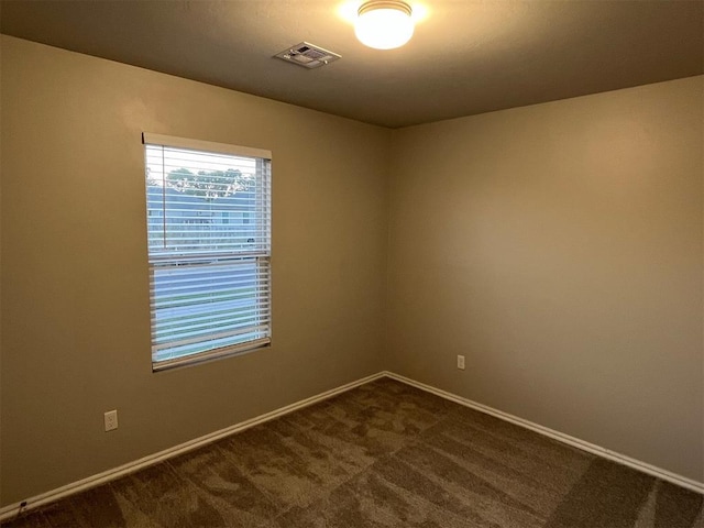unfurnished room featuring dark colored carpet, baseboards, and visible vents