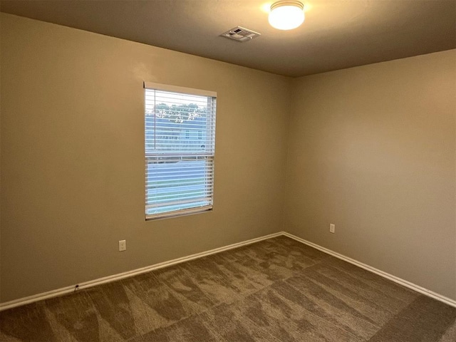 spare room featuring baseboards, dark colored carpet, and visible vents