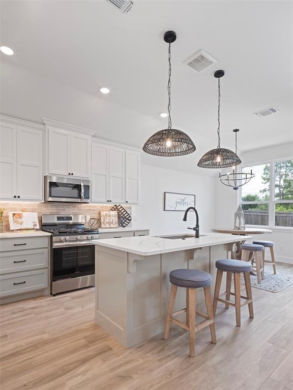 12712 NW 1st Ct, Yukon, OK 73099 - kitchen featuring stainless steel appliances, an island with sink, decorative backsplash, light wood finished floors, and a sink