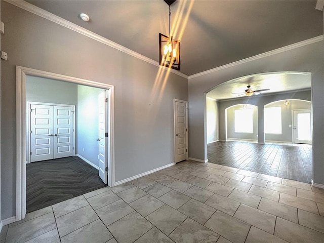 spare room with arched walkways, baseboards, crown molding, ceiling fan, and a smoke detector