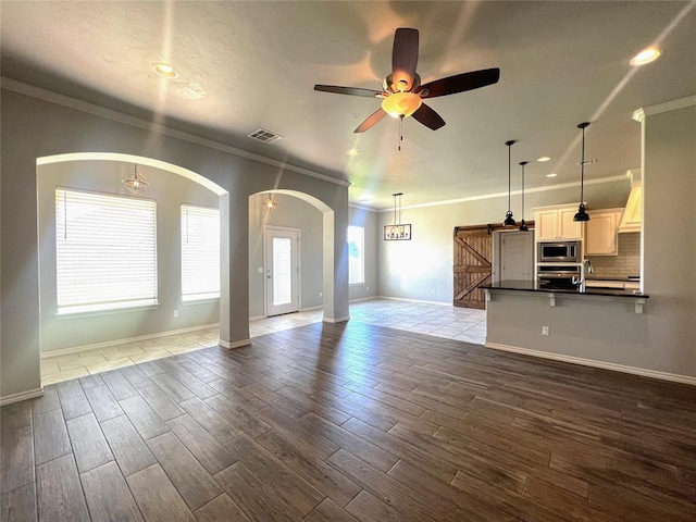 unfurnished living room with crown molding, a ceiling fan, arched walkways, baseboards, and dark wood-type flooring