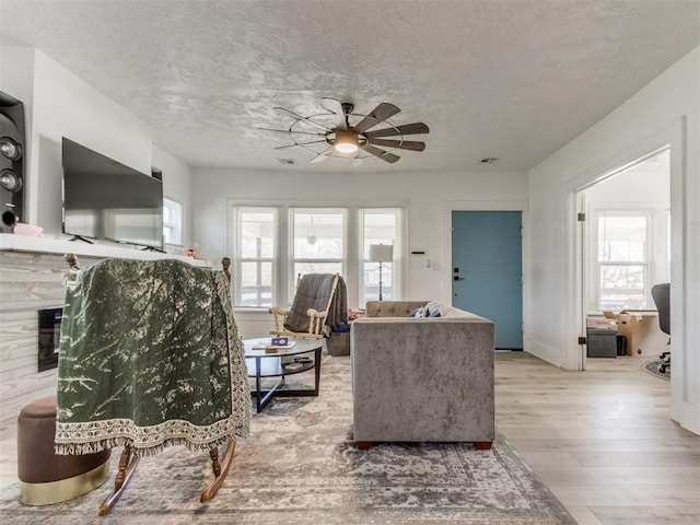 living area with a fireplace, wood finished floors, a textured ceiling, visible vents, and ceiling fan