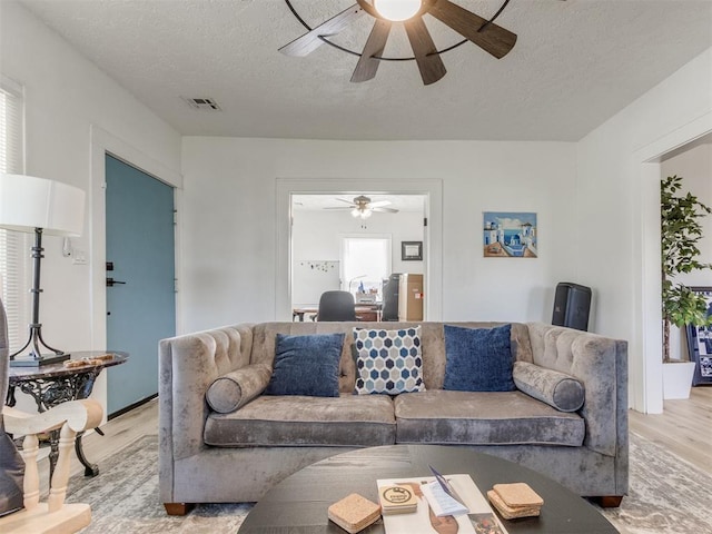 living room with a ceiling fan, a textured ceiling, light wood-style floors, and visible vents