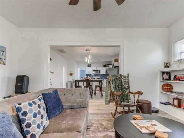 living area with a textured ceiling, ceiling fan, visible vents, and light wood-style floors