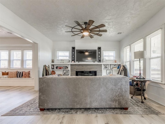 living area with a textured ceiling, visible vents, a ceiling fan, a fireplace, and wood finished floors