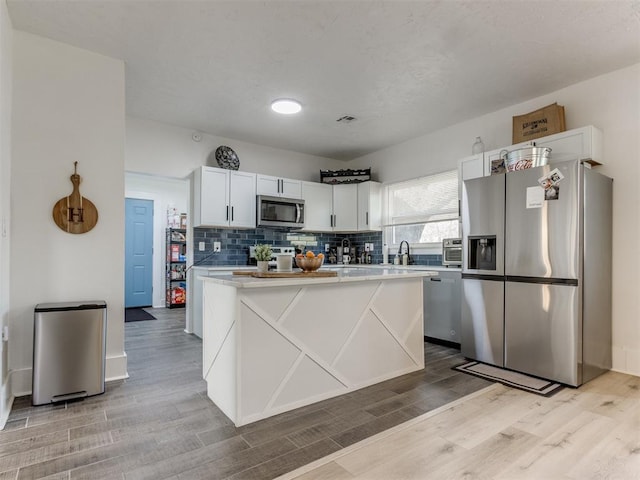 kitchen with white cabinetry, light countertops, backsplash, light wood finished floors, and appliances with stainless steel finishes