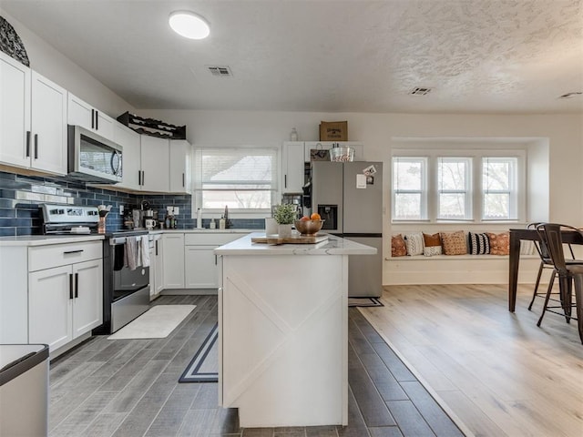 kitchen featuring a center island, decorative backsplash, visible vents, appliances with stainless steel finishes, and wood finished floors