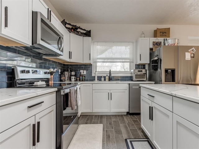 kitchen with wood tiled floor, a sink, appliances with stainless steel finishes, and decorative backsplash
